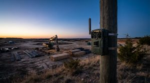 Caméra de chasse fixée à un poteau en bois surveillant un chantier de construction au coucher du soleil.